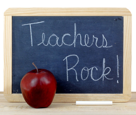 Rough textured blackboard with wooden frame. A red apple and a stick of white chalk sit in front....