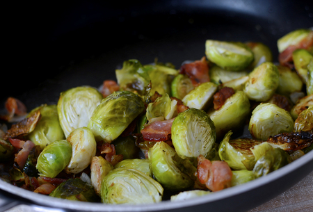 Closeup of roasted brussel sprouts with bacon and shallots in a frying pan. Green is the dominant color of this vegetable with red accents from the meatの写真素材