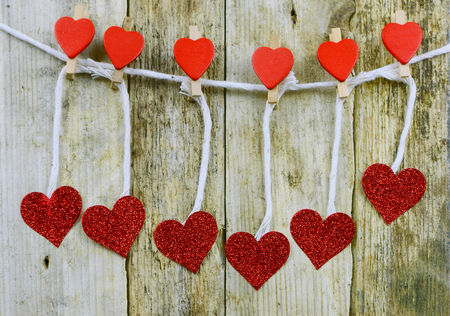 Sparkly red hearts handing from decorated clothespins by string in front of rustic wooden background for Valentine's Dayの写真素材