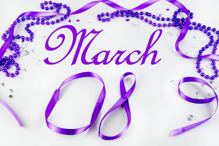 Purple beads and ribbon and sparkly jewels on a light background make a border for International...