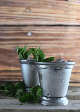 Image for Kentucky Derby in May showing two silver mint julep cups with crushed ice and fresh mint in a rustic setting, vertical, copy spaceの写真素材