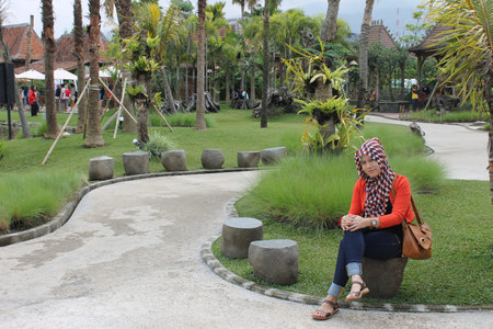 Lembang, Indonesia - Jan 22, 2023 : A woman in a hijab is sitting on a stone path in the park.のeditorial素材