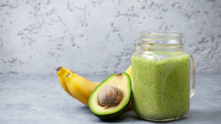 Healthy green smoothie with banana and avocado in glass jar on concrete background