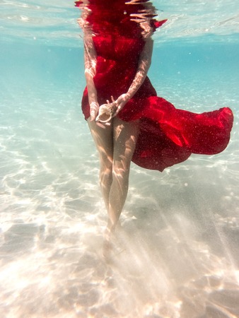 Underwater in the sea with the purest water. Beautiful girl in a scarlet dress and flowing hair.の写真素材
