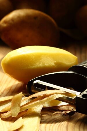Peeled potato and skin with a potato peeler on a wood backgroundの写真素材