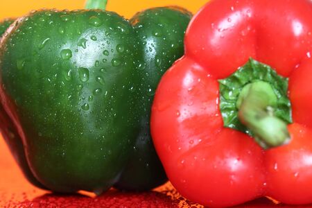 Red and green peppers with water droplets on an orange backgroundの写真素材