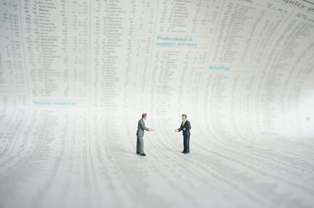 Miniature scale model businessmen standing on shares page of a newspaper.の写真素材