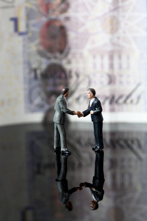 Miniature scale model business figures standing in front of a twenty pound note sterling.