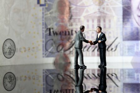 Miniature scale model business figures standing in front of a twenty pound note sterling.の写真素材