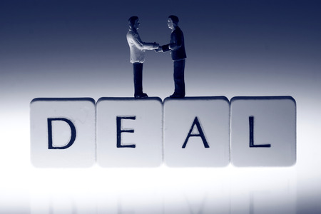 Miniature scale model businessmen on tiles spelling deal shaking hands.の写真素材