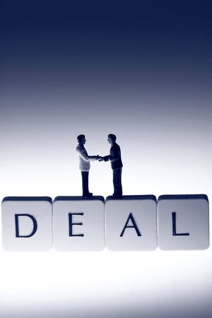 Miniature scale model businessmen on tiles spelling deal shaking hands.の写真素材