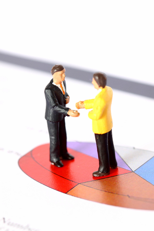 Miniature scale model businessmen shaking hands on pie chart.の写真素材