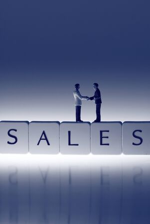 Miniature scale model businessmen on tiles spelling sales shaking hands.の写真素材