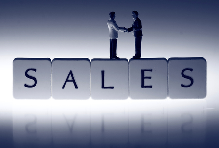 Miniature scale model businessmen on tiles spelling sales shaking hands.の写真素材
