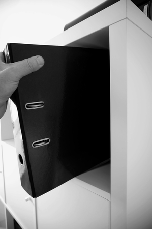 Man taking a binder folder from a shelfの写真素材