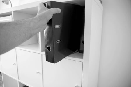 Man taking a binder folder from a shelfの写真素材