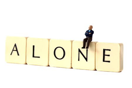 Miniature scale model senior male pensioner sitting on tiles spelling aloneの写真素材