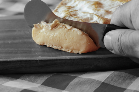 Man cutting a slice of Somerset Brie with a cheese knife with selective colorの写真素材
