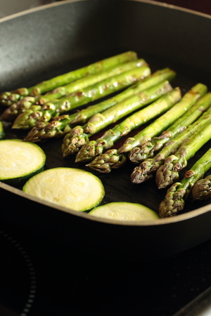 Asparagus and sliced courgette zucchini cooking in a griddle frying pan on a hob stoveの写真素材
