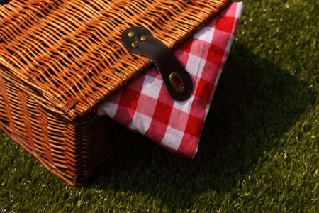 Wicker picnic basket with a red and white gingham cloth on a grass background