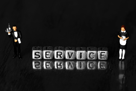 Service on beads with a scale model waiter and waitress standing next to word on wooden backgroundの写真素材