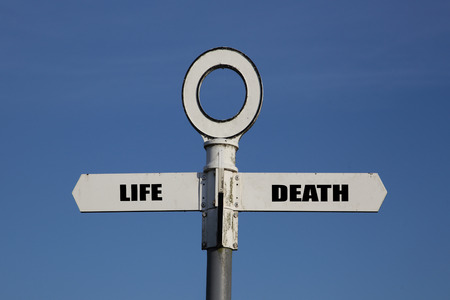 Old road sign with life and death pointing in opposite directions against a blue skyの写真素材