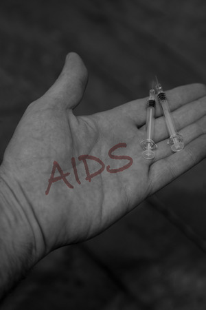 Man holding syringes needles with the word aids written on his hands with selective colourの写真素材