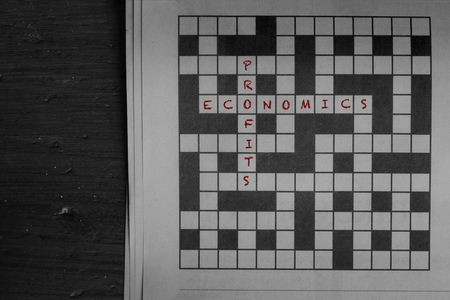 Economics and profits written in red as solutions to a newspaper crossword puzzle on woodの写真素材