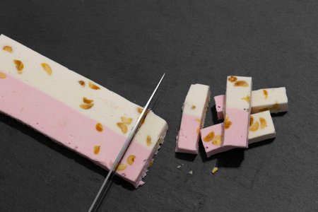Pink and white nougat with peanut being cut with a knife on a slate surface