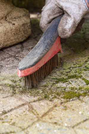 Man wire brushing garden patio concrete slabs to remove moss and lichen from them.  Household chore concept.の写真素材