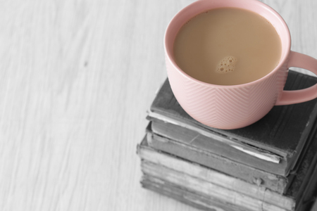 Cup of tea in a pink cup on a stack of old antique books with selective colour on a grey wood backgroundの写真素材