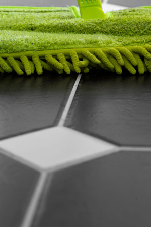 Cleaning tiled floor with a green dry mop head.  Selective colour image.