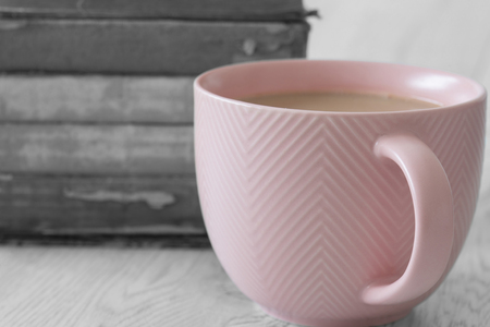 Cup of tea in a pink cup on a stack of old antique books with selective colour on a grey wood backgroundの写真素材