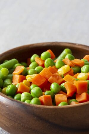 Mixed vegetables, with carrot, beans, peas and sweet corn,  in a wooden bowl.  On a grey textured cotton tableclothの写真素材