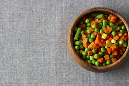Mixed vegetables, with carrot, beans, peas and sweet corn,  in a wooden bowl.  On a grey textured cotton tableclothの写真素材