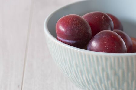 British organic plums, freshly picked, in a pastel green bowl dish. Grey wood backgroundの写真素材