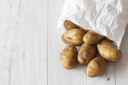New potatoes in a white paper bag, environmentally friendly biodegradable packaging, with a grey wood backgroundの写真素材