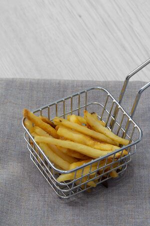 Fries chips in a wire mesh basket with a handle.  Standing on a grey marl tea towel and a grey wood background.の写真素材