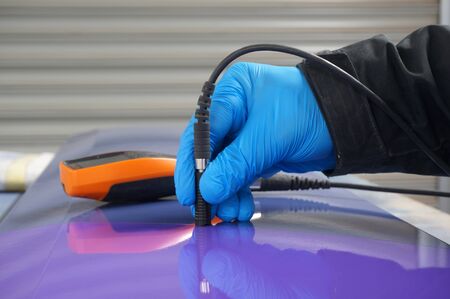 Person using probe, with digital tester, to measure the paint thickness microns on a painted metal panel. Person wearing protective gloves.の写真素材