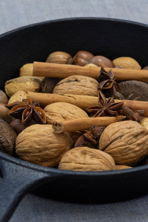 Walnuts, hazelnuts, Brazil nuts and walnuts in a cast iron frying pan with cinnamon sticks and star...