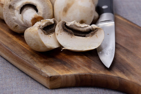 Closed cup white mushrooms on a wooden chopping board.  On a grey tablecloth