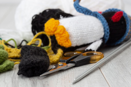 Knitted parts for woolen penguin toy with scissors and knitting needles.  On a grey wood surface. ...