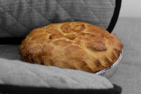 Homemade freshly baked Bramley apple pie beimg put on a tablecloth by a person wearing oven gloves