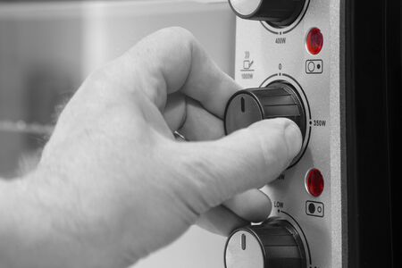 Man setting the power setting on an electric oven grill by turning a dial.  With selective colourの写真素材
