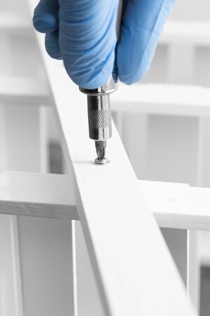 Man assembling a white flat pack ladder shelving unit with a screwdriver.  Flat pack assembly conceptの写真素材