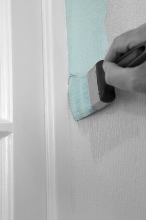 Man painting wall with mint green paint on textured wallpaper,  cutting in against door frame.  With selective colourの写真素材