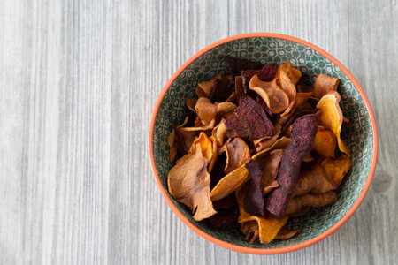 Sweet potato, beetroot and parsnip crisps chips in a patterned bowl.  Grey wood backgroundの写真素材