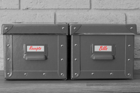 Storage boxes with receipts and bills written on labels in red.  With a grey brick background