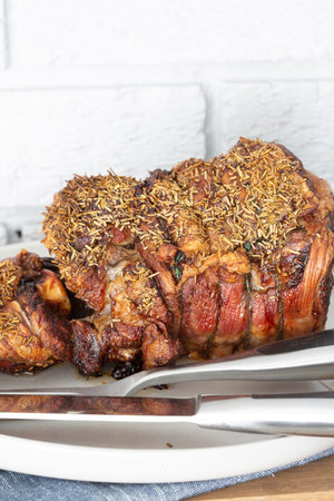 Roast leg of lamb with rosemary on a plate.  Grey brick background