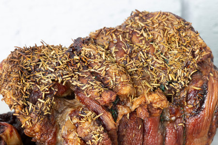 Roast leg of lamb with rosemary on a plate.  Grey brick background